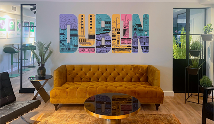 La oficina de Sprout Social en Dublín, que muestra un área de descanso con un sofá, dos pequeñas mesas de café y un mural.​​ 