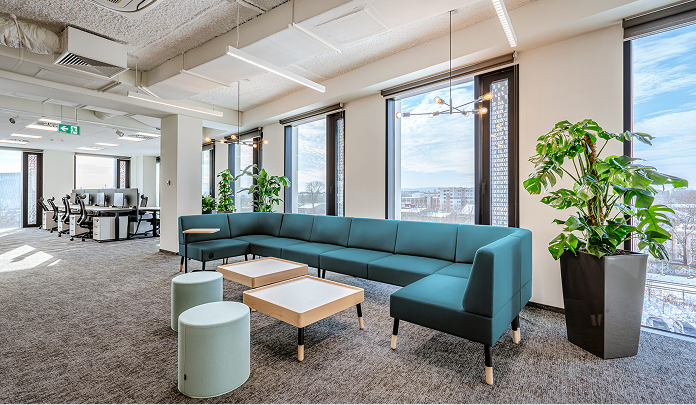 La oficina de Sprout Social en Polonia, que muestra un salón con un sofá y mesas, rodeado de grandes ventanales y plantas.​​ 